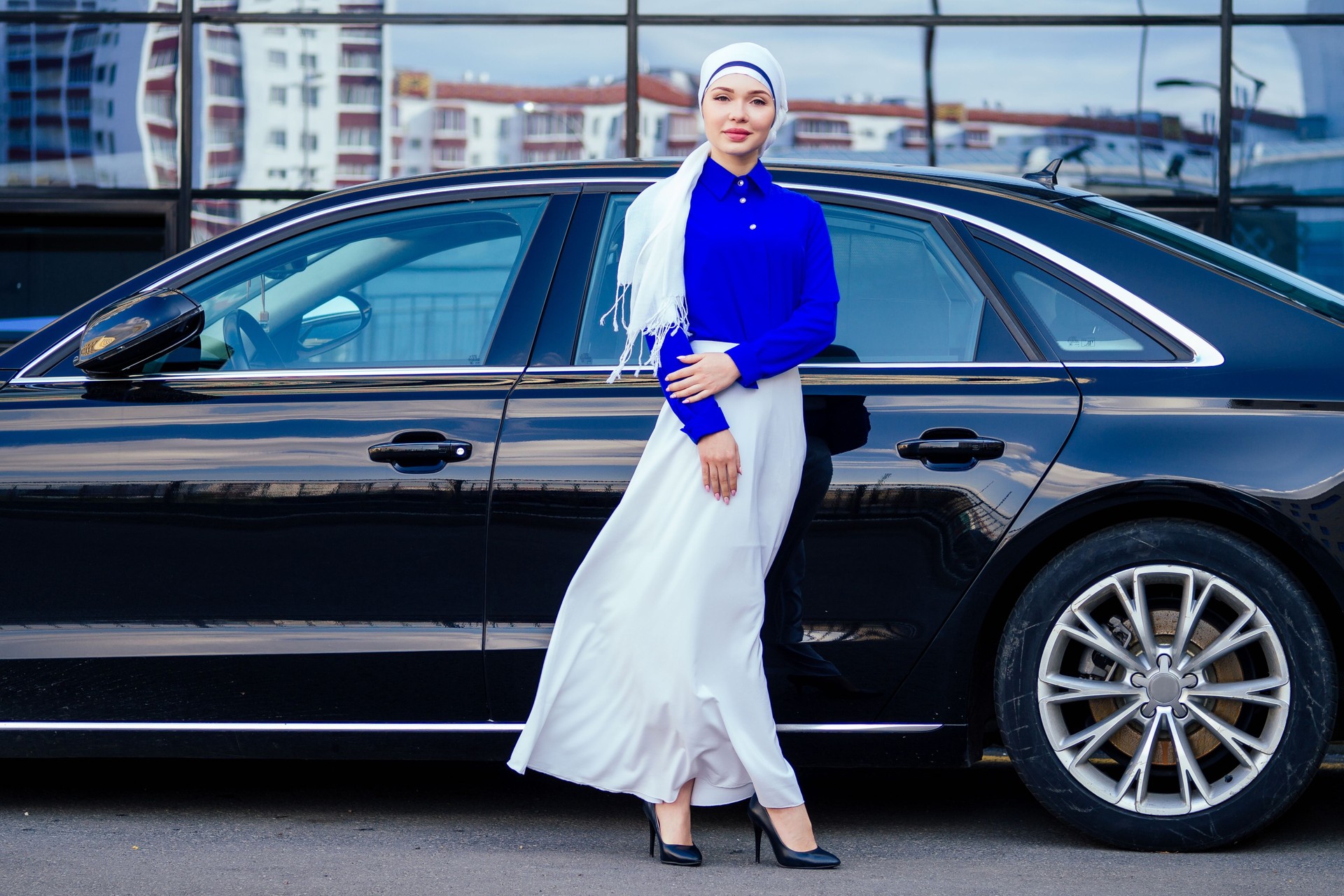 Arab business woman hijab standing in front of her luxury car on the street on a background of skyscrapers of Dubai. The woman is dressed in a stylish abaya
