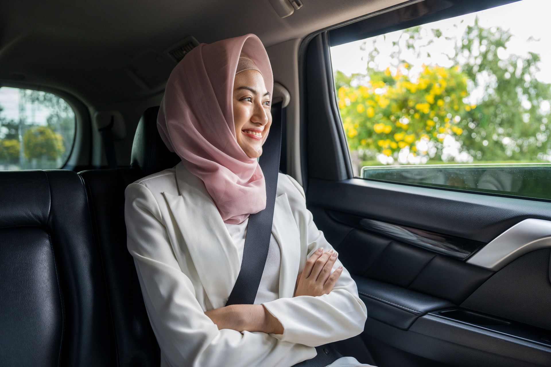 Asian muslim woman traveler sitting in car back seats call taxi service put on safety belt. Female islamic passenger in car traveling to destination.